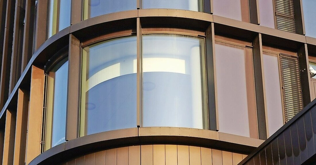 Bürogebäude mit einer Fassade aus Kupferprofilen, gebogenem Glas und integriertem Sonnenschutz.